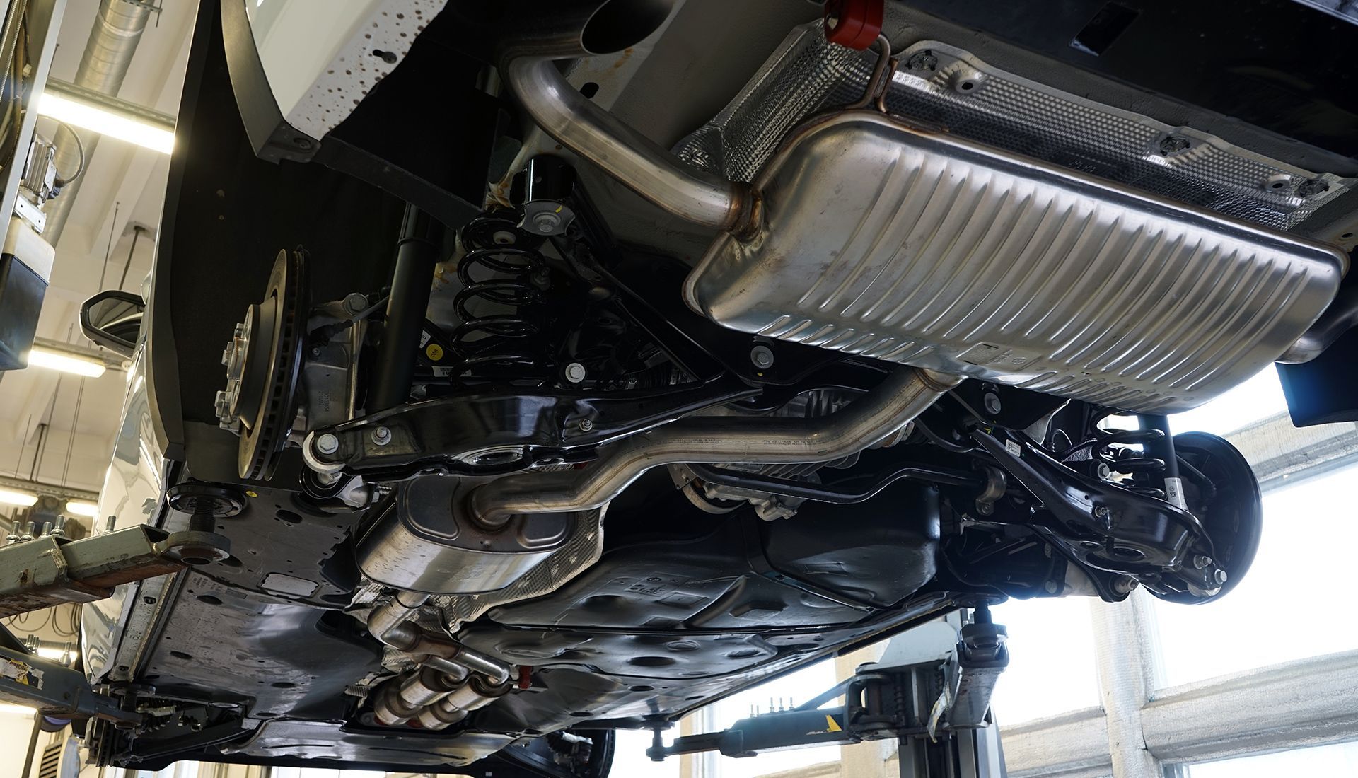 Undercarriage of a car on a lift, showing exhaust system and suspension components.
