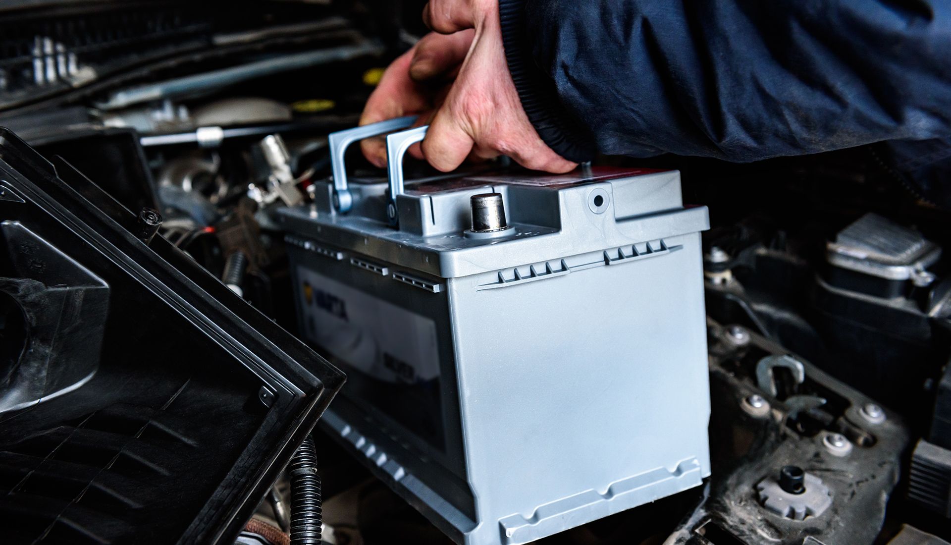 Hand installing car battery in engine compartment.