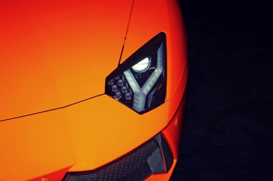 Close-up of an orange sports car’s front headlight and hood against a dark background