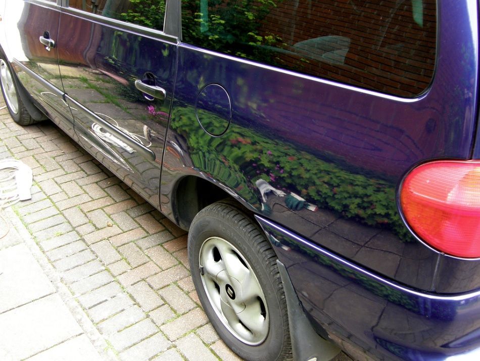 Dark blue minivan parked on a brick driveway, side view showing rear wheel and red taillight