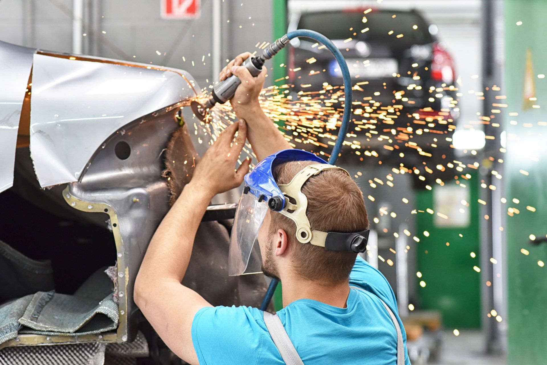 A mechanic cutting the body of a car with sparks flying over his head