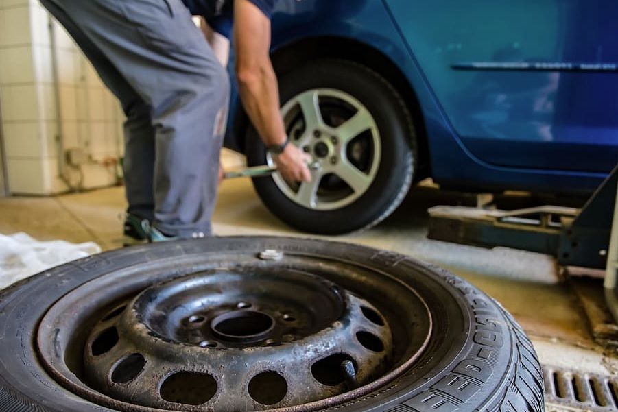 Mechanic replacing a car tire beside a blue vehicle, with a spare wheel in the foreground.