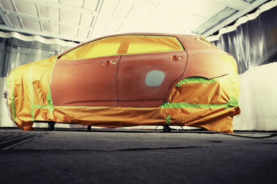 Orange car covered in masking paper and plastic inside a paint booth