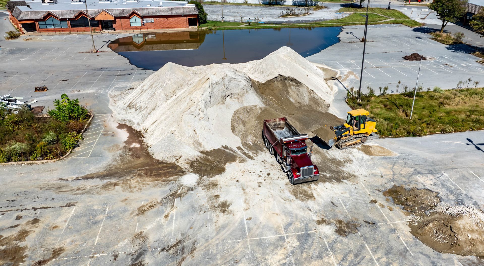 Large white sand pile beside a red dump truck in an industrial yard