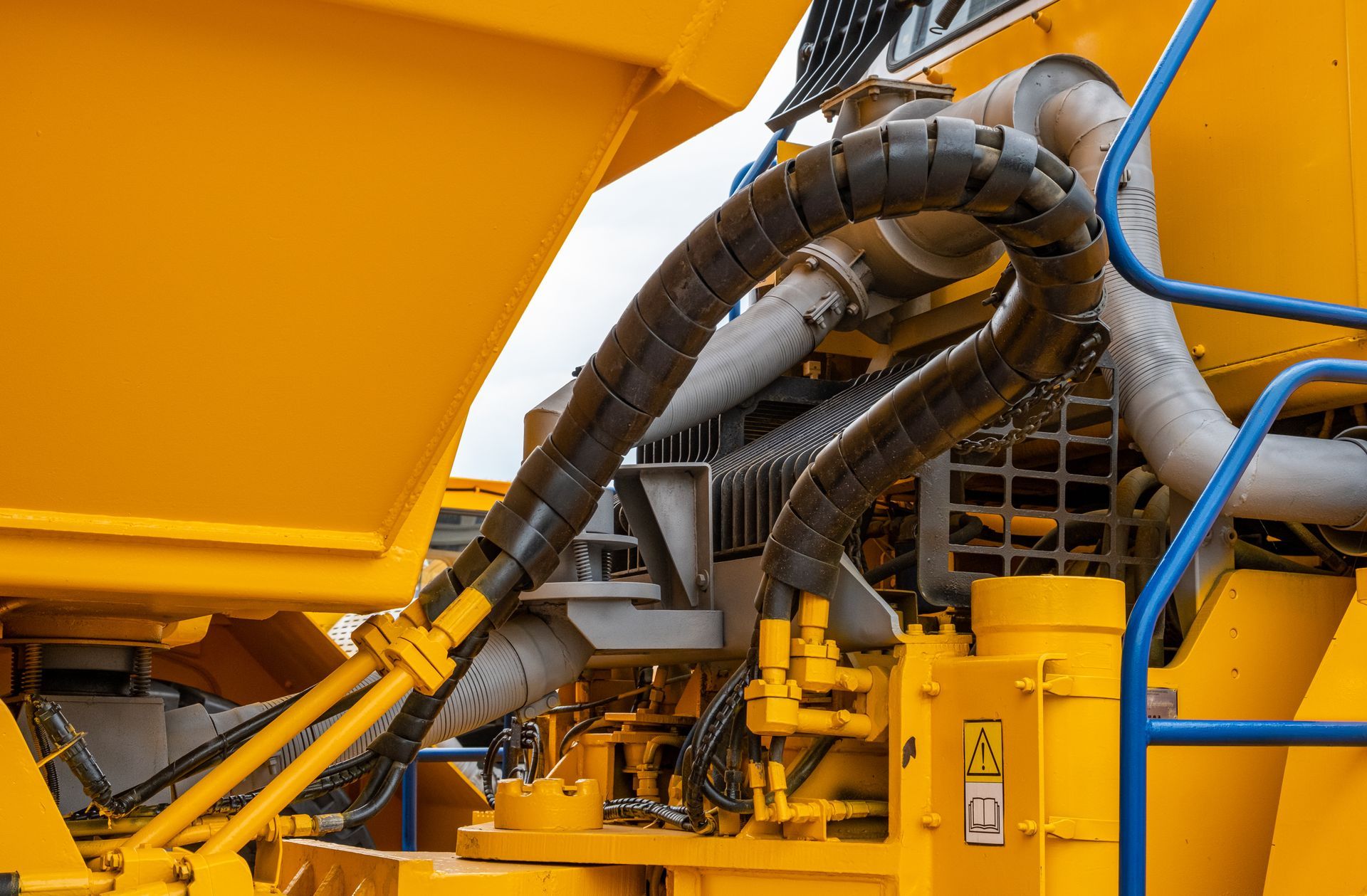 Yellow industrial machinery with thick black hoses and blue railings in a factory setting