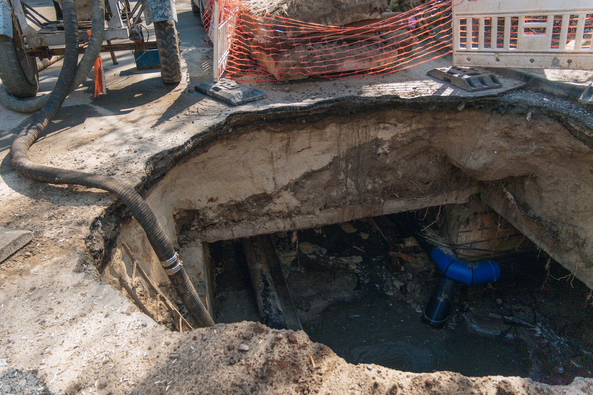 Large underground excavation pit with exposed soil and a worker in blue inside, surrounded by safety fencing