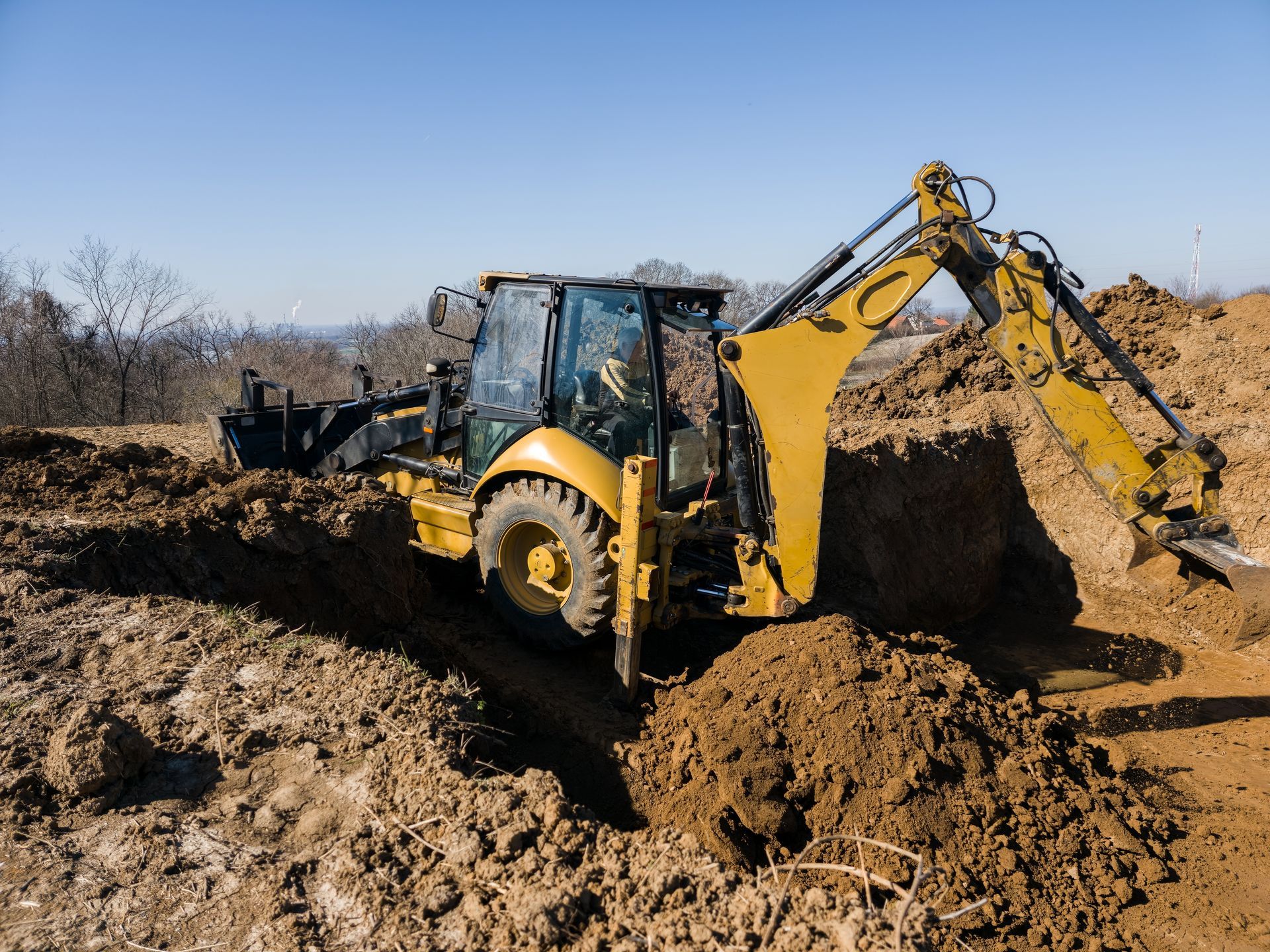 Yellow backhoe loader digging dirt at a construction site under a clear sky