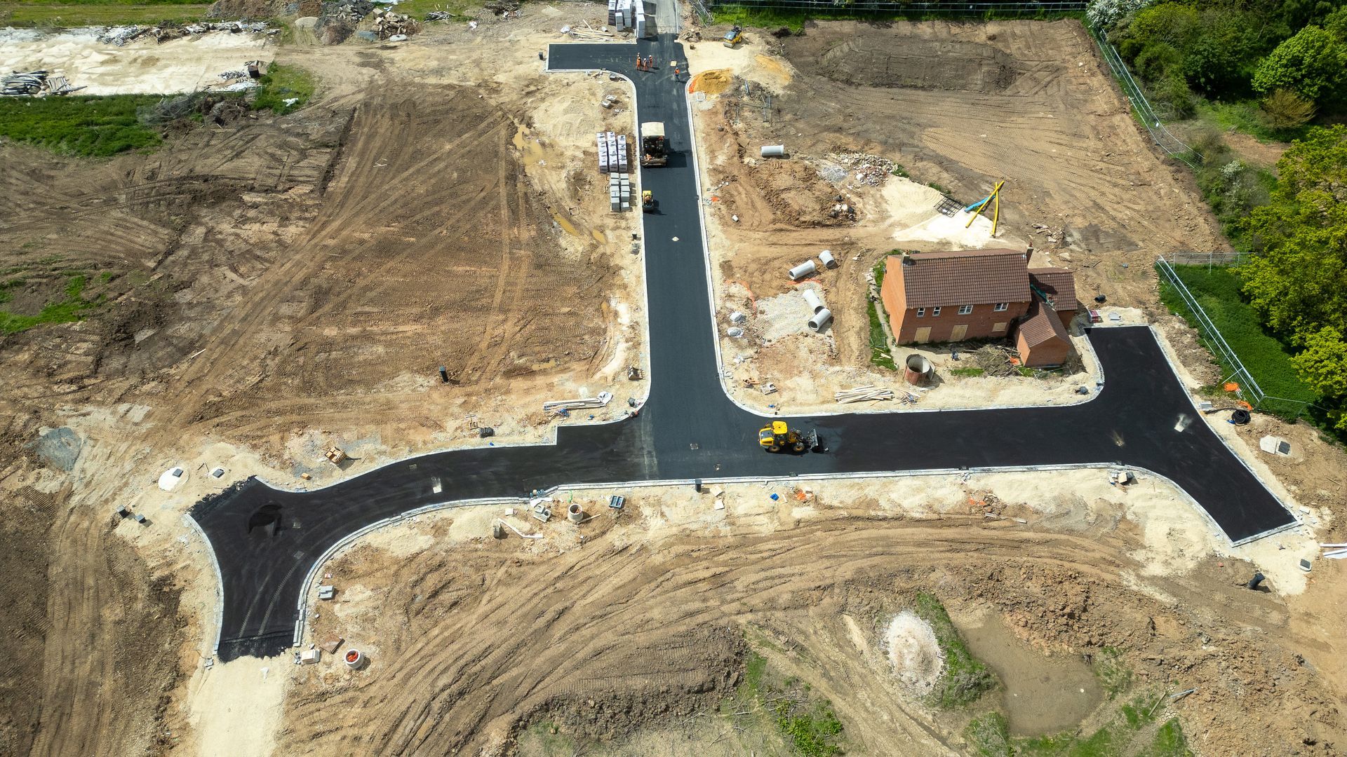 Aerial view of a new suburban road network under construction beside cleared lots and a house