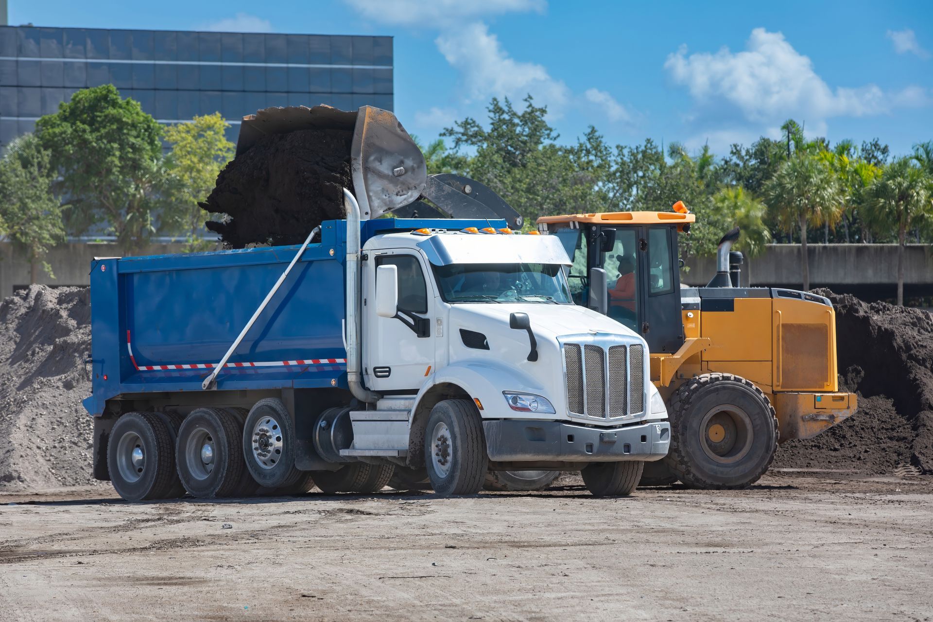 Dump truck and front loader at a dirt worksite with a pile of gravel or soil.
