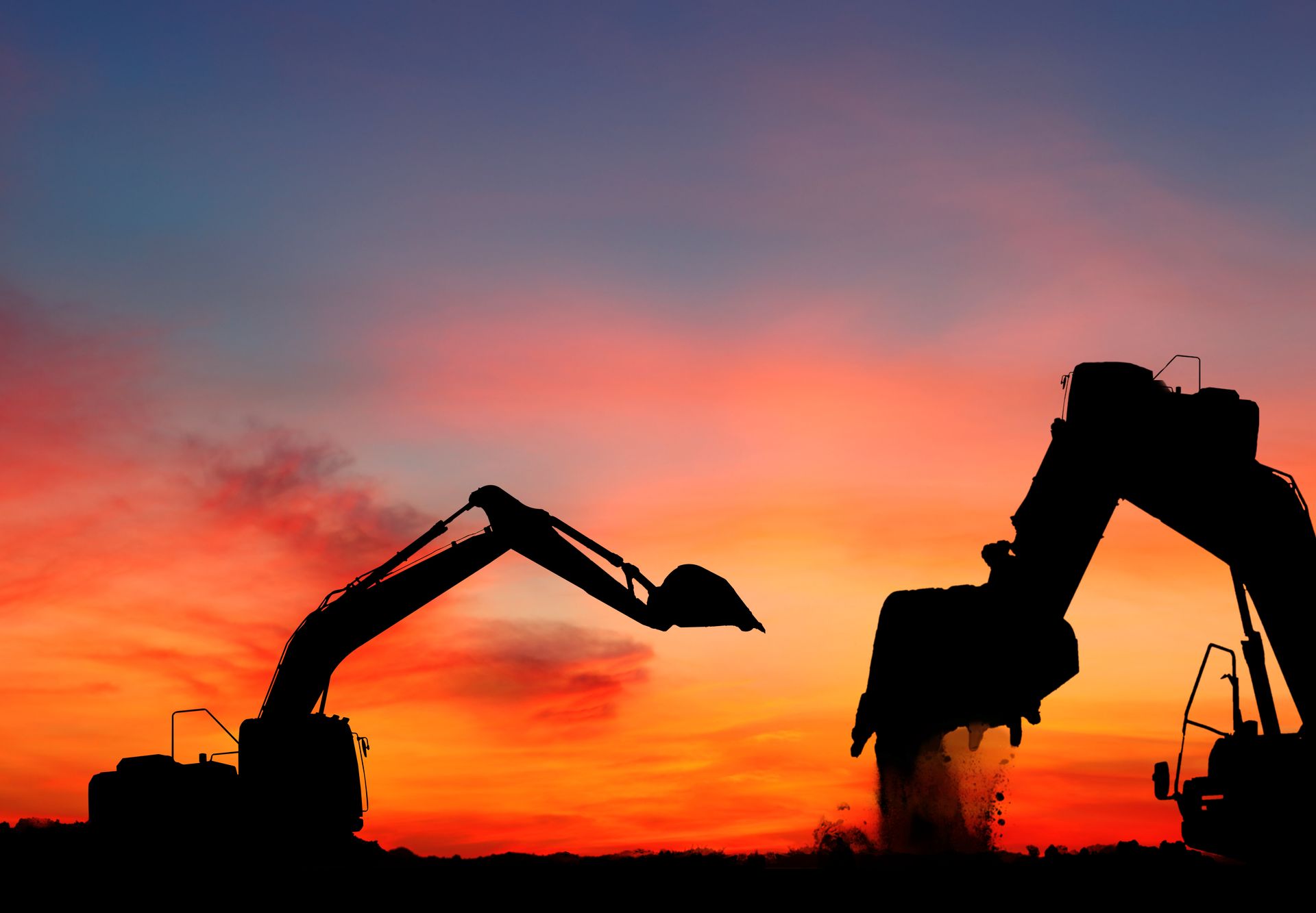 Silhouettes of two excavators against a vivid orange-red sunset sky