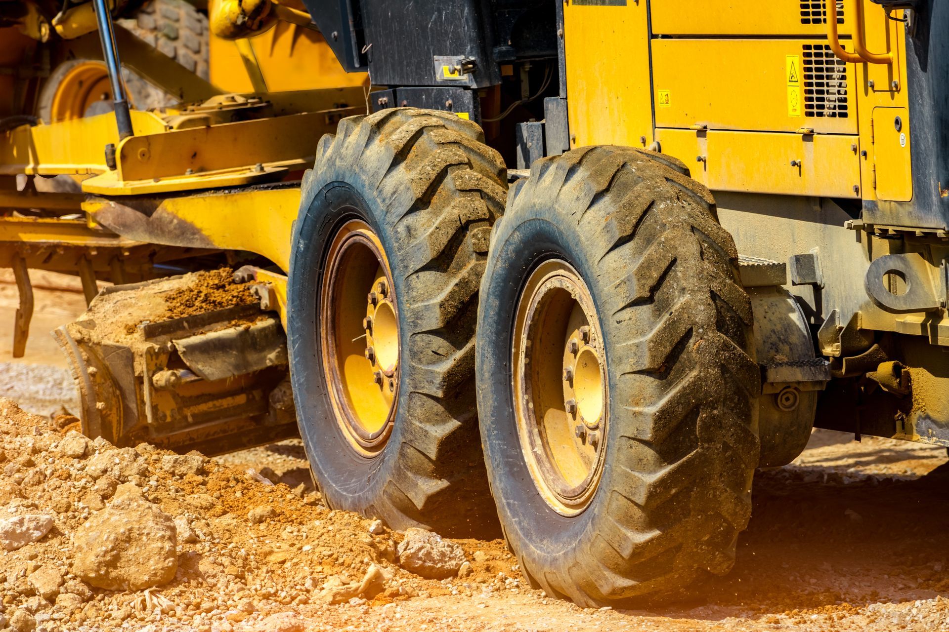 Yellow construction vehicle with large tires grading a dirt surface