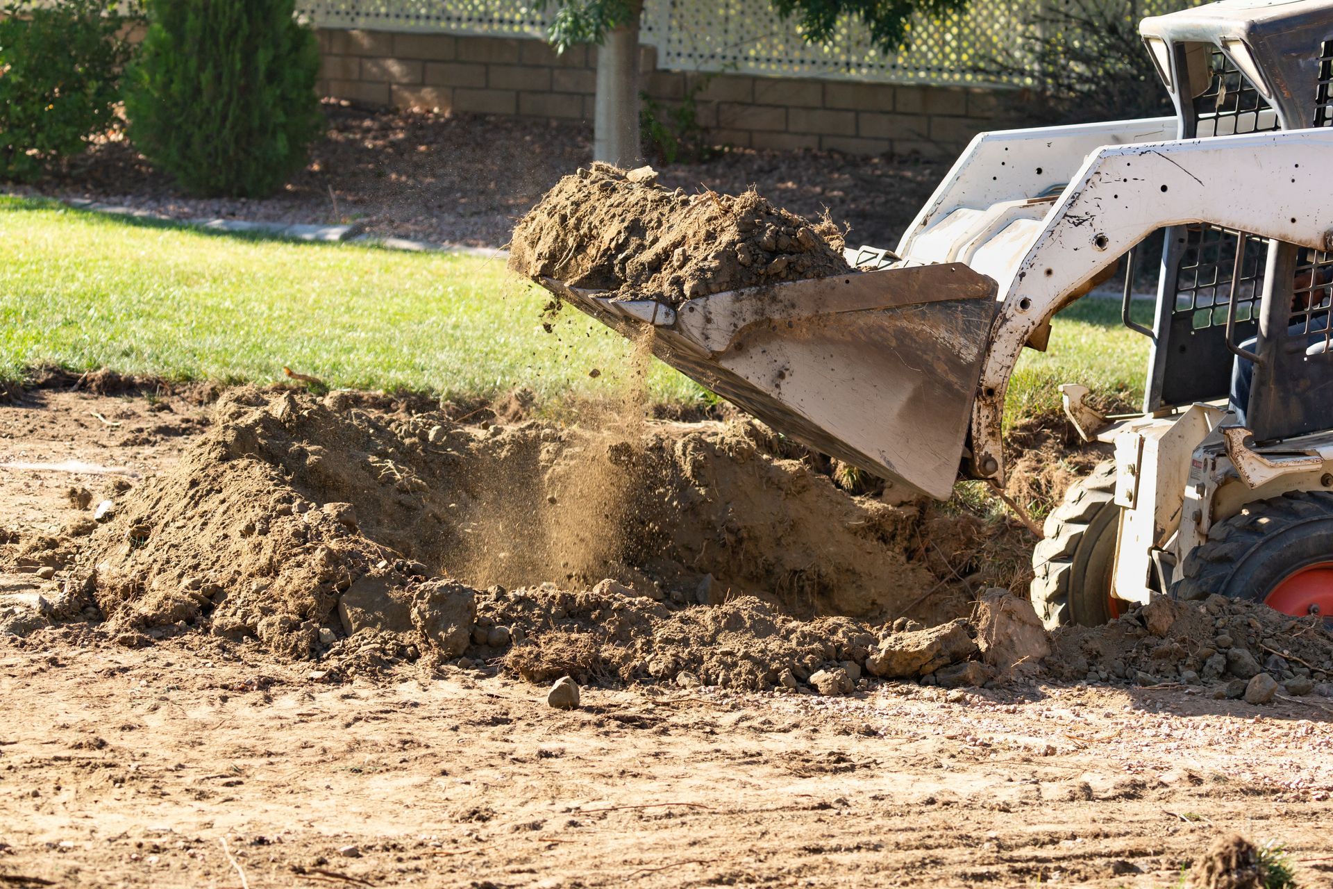 Front loader scooping dirt at a construction site near a grassy edge