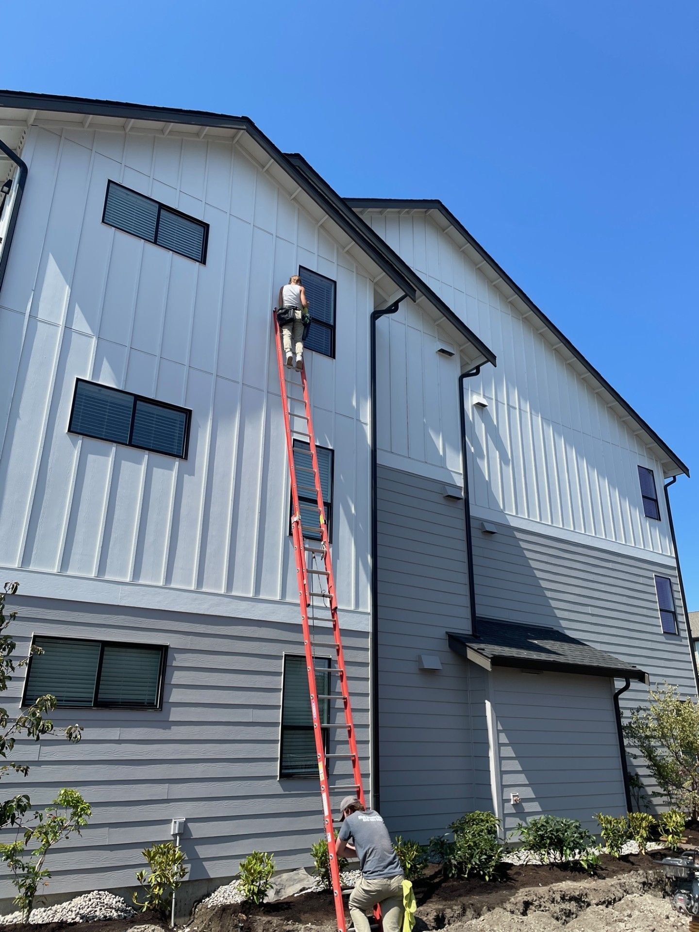 A man is standing on a ladder painting the side of a house.