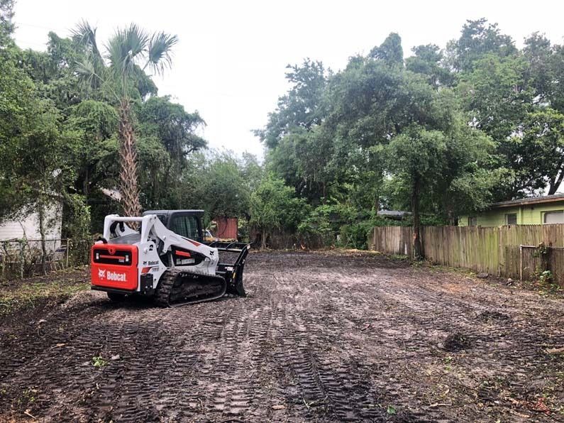 White mini excavator on muddy ground in a tree-lined yard after rain