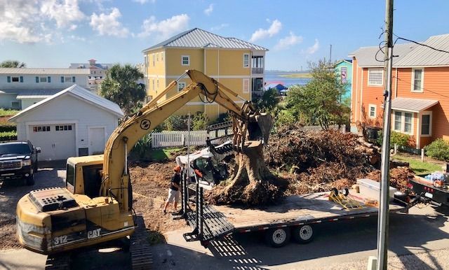 Excavator loading a tree stump onto a flatbed trailer in a residential neighborhood