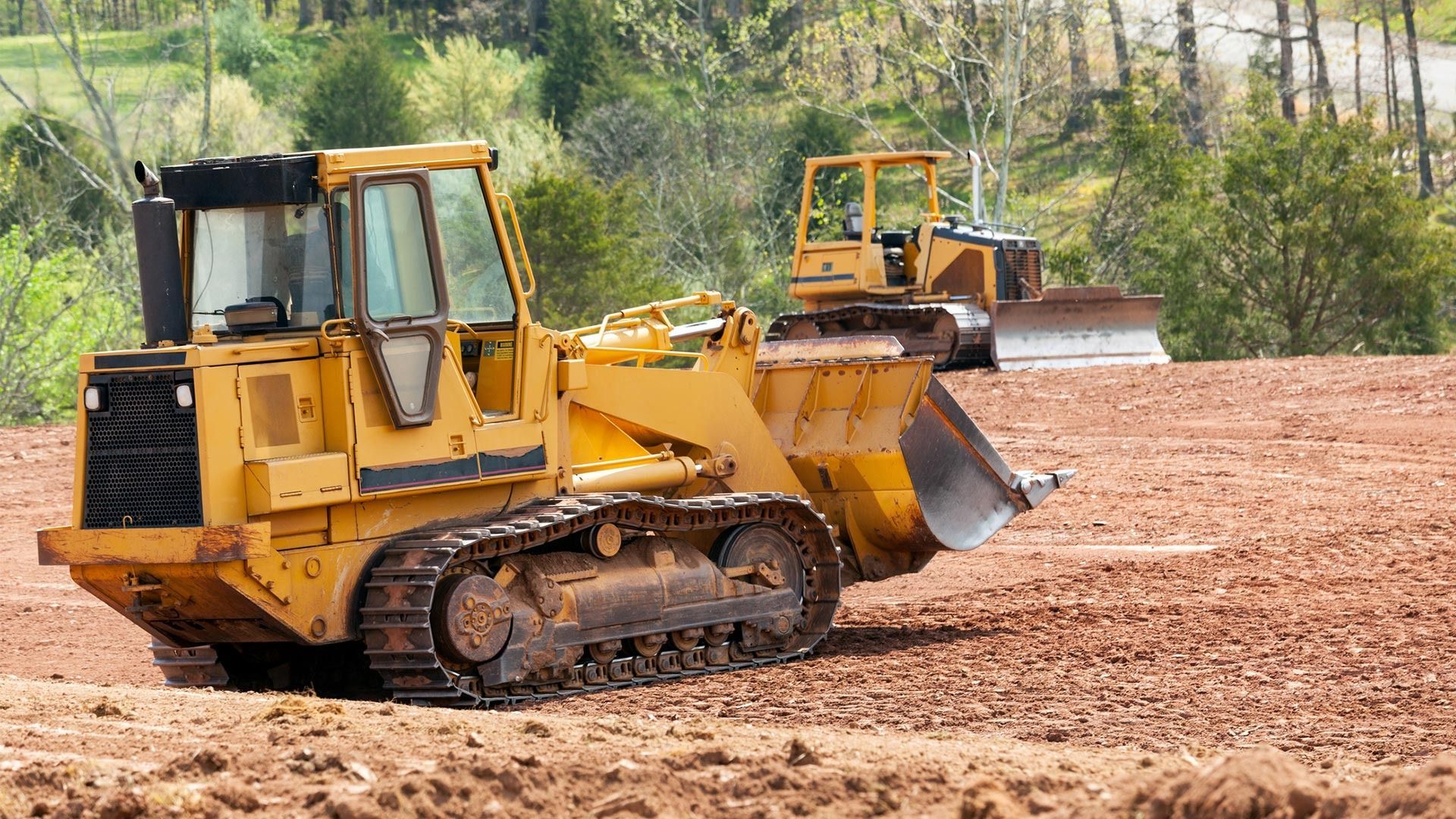 Yellow bulldozer grading a dirt field, with another construction vehicle in the background.