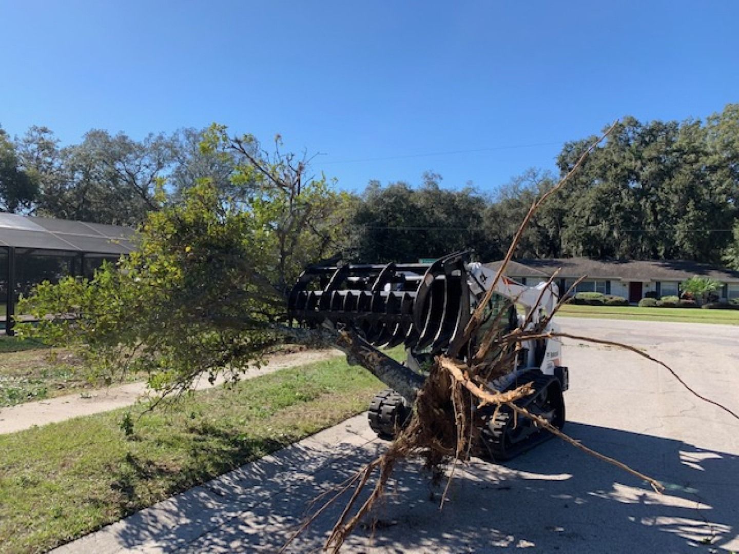 Overturned utility trailer blocking a suburban street, with a broken tree branch tangled in the metal frame.