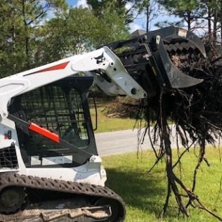 White skid steer lifting tangled roots with its bucket in a grassy yard near a road and trees