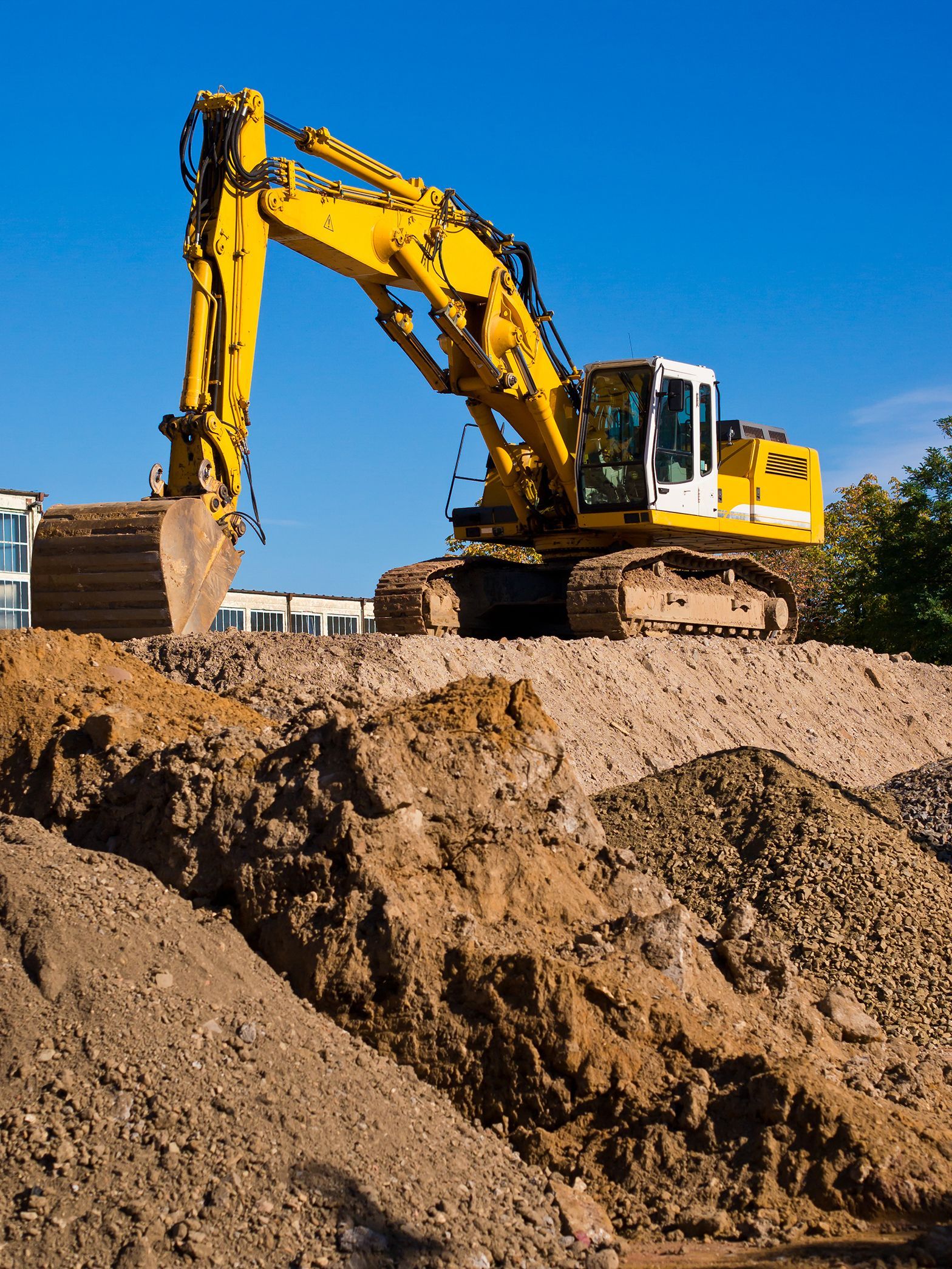 Yellow excavator digging a dirt mound at a construction site under a clear blue sky
