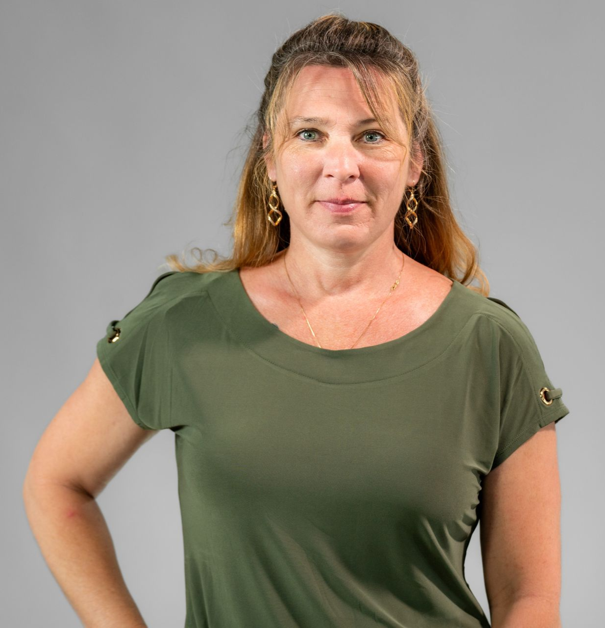 Woman with long hair in a green shirt, posing with her hand on her hip.