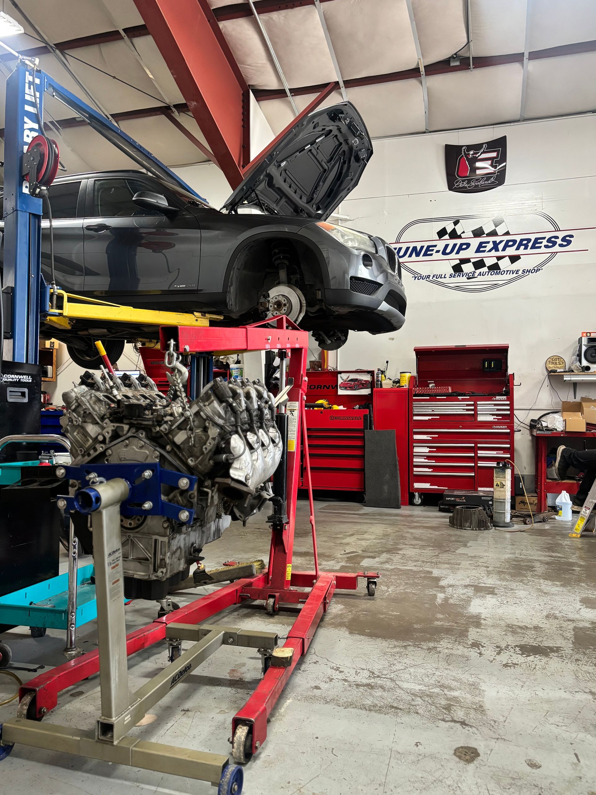 Black race car on lift in auto shop, engine exposed, red tool cabinets in background  | Tune-Up Express Auto
