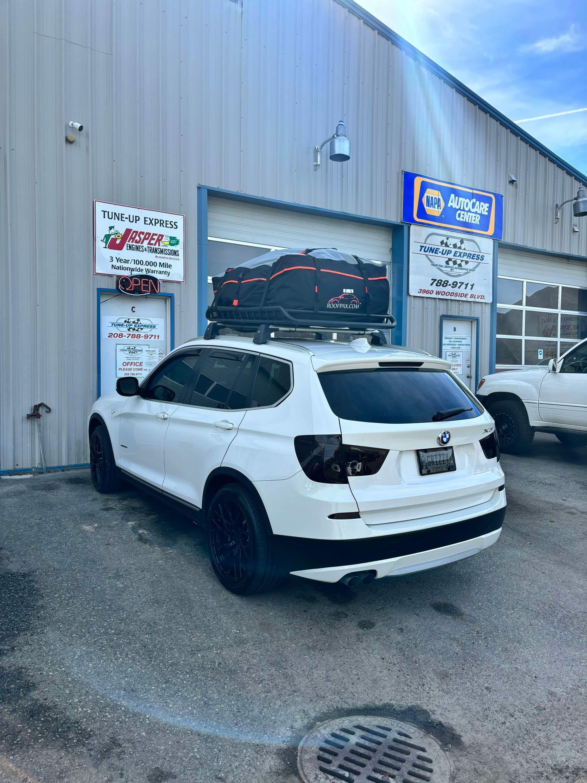 White SUV parked outside an auto repair shop with signs on a metal building.  | Tune-Up Express Auto