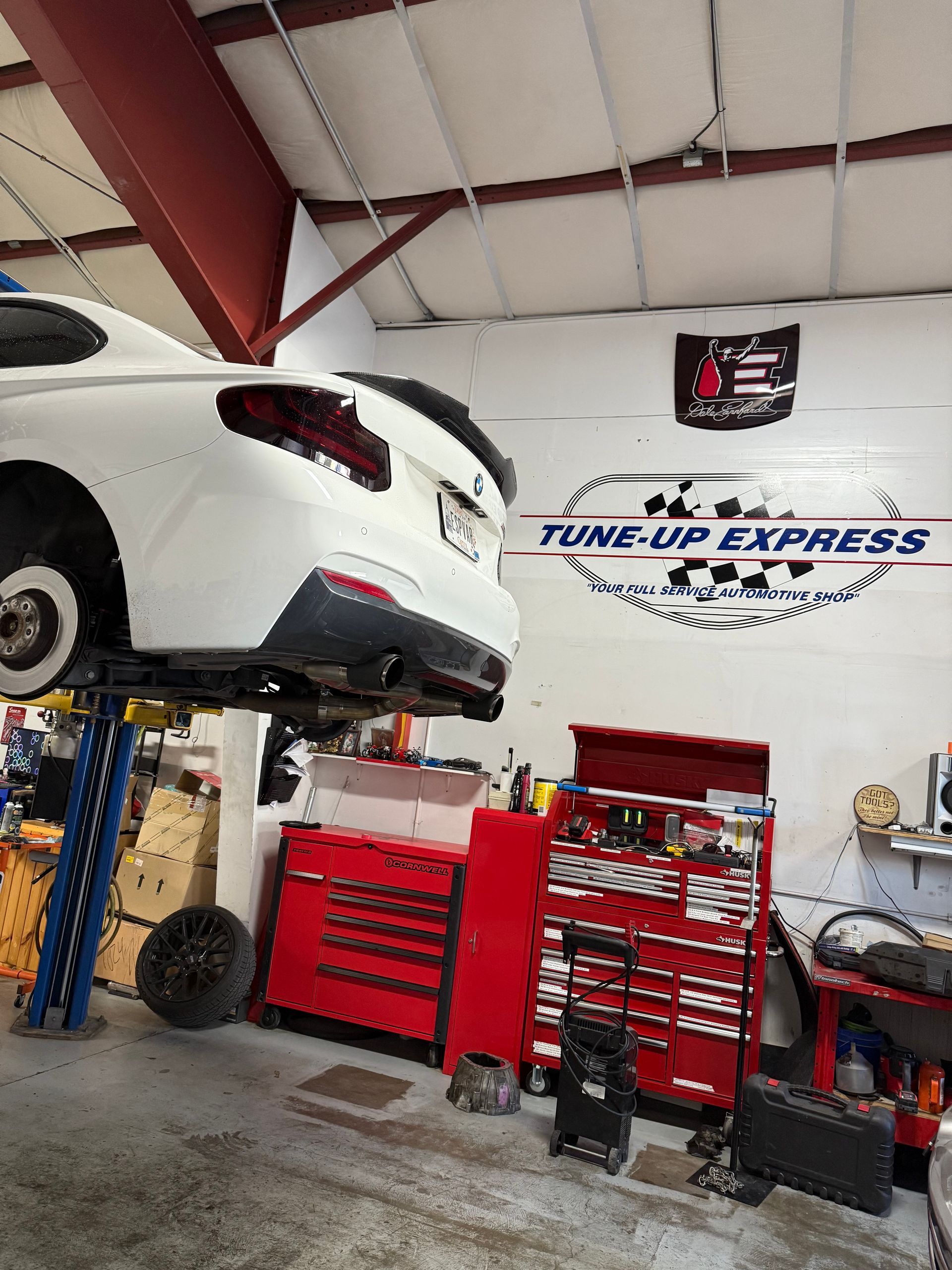 White sports car lifted in an auto repair shop with red tool cabinets and a Tune-Up Express sign.  | Tune-Up Express Auto