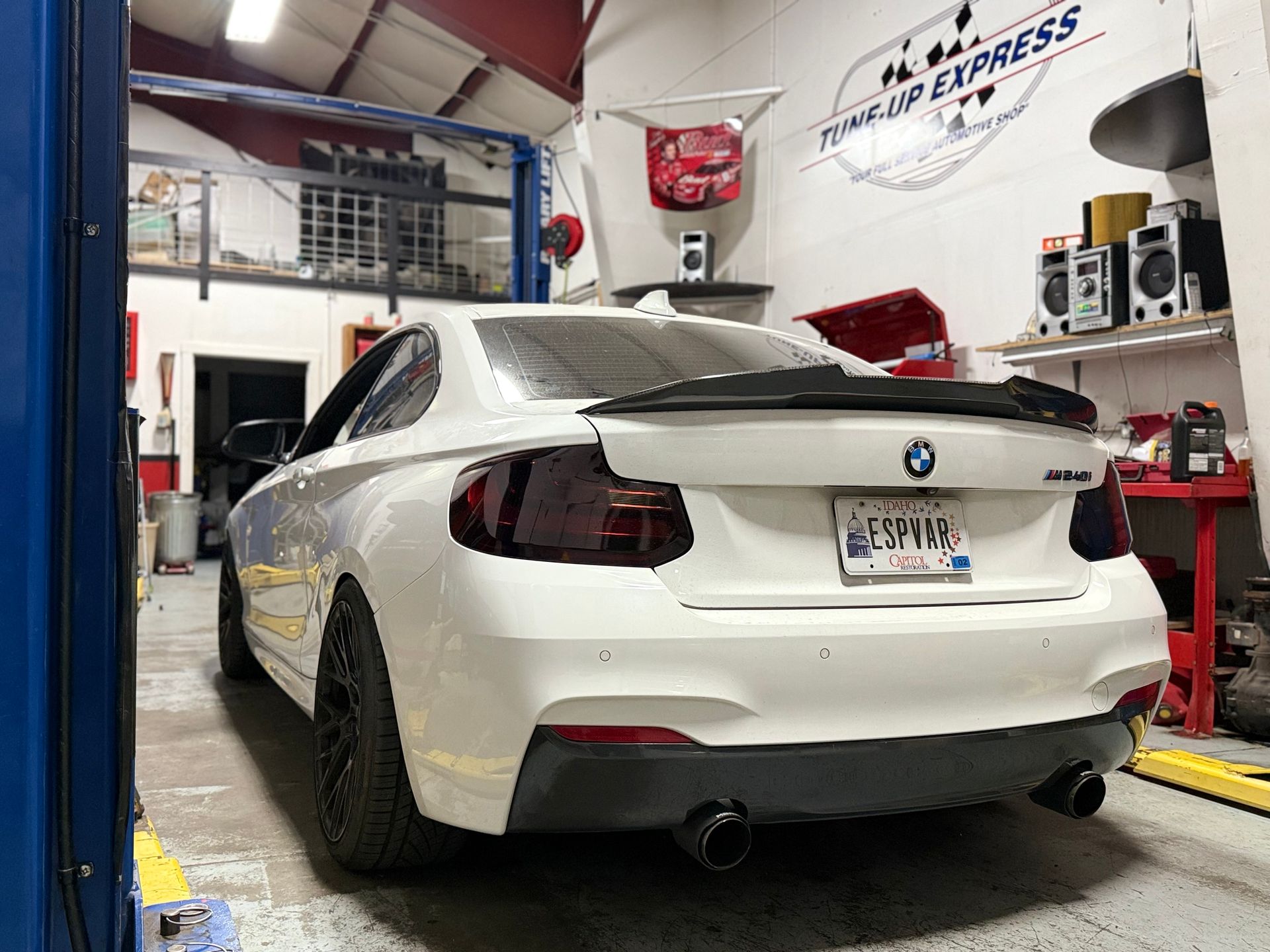 White BMW coupe in an auto shop, rear view, with red lift and tools around it  | Tune-Up Express Auto