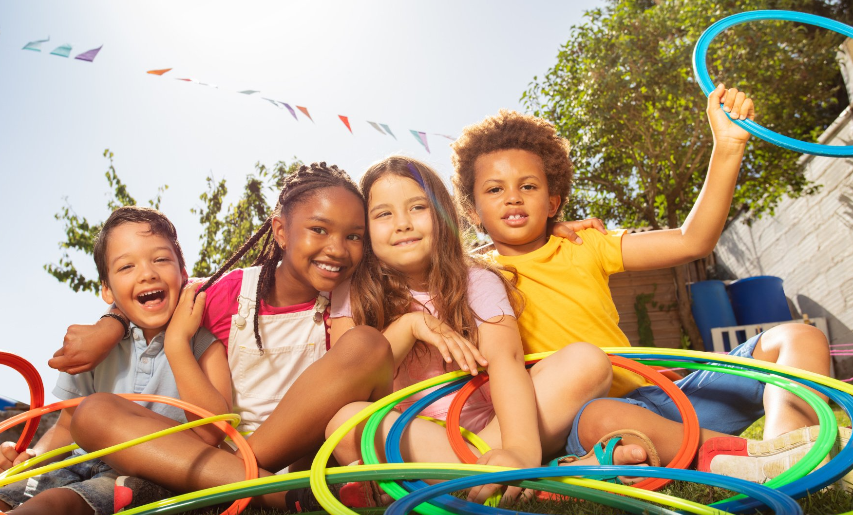 A group of children are sitting on the grass with hula hoops.