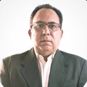 Hombre con gafas y blazer sobre un fondo blanco, mirando directamente a la cámara.