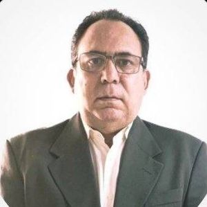 Hombre con gafas y blazer sobre un fondo blanco, mirando directamente a la cámara.