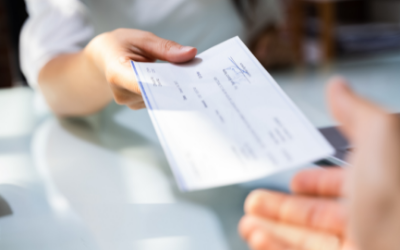 Hands exchanging a white check or document over a softly lit table.