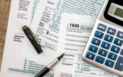 Tax forms, pens, and a calculator on a desk for tax preparation