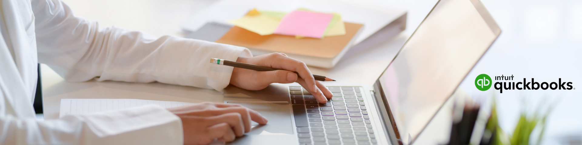 Hands typing on a laptop at a desk with papers and sticky notes nearby