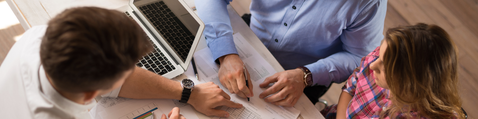 Three coworkers leaning over a laptop and documents, discussing work at a table.