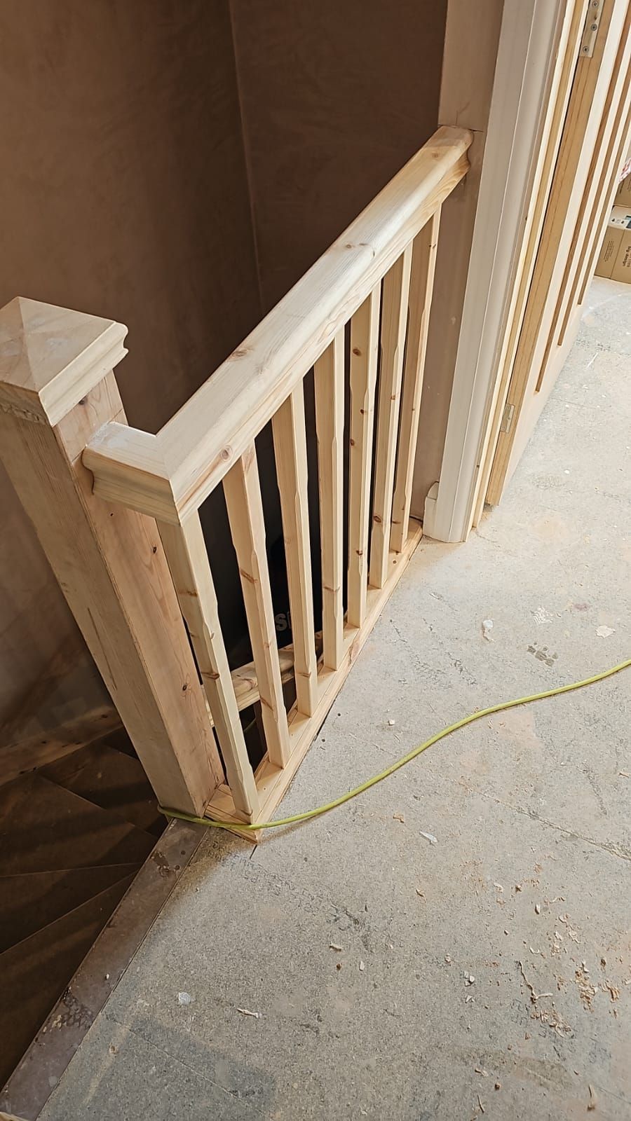 A wooden railing is being built on a staircase in a house.