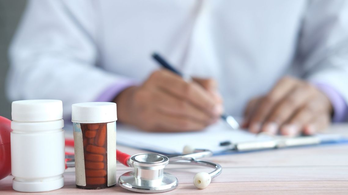 Doctor writing notes behind medicine bottles and a stethoscope on a desk