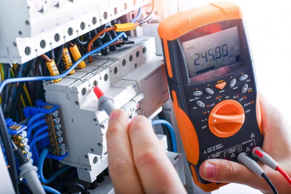 A person is holding a multimeter in front of an electrical box. — KARM Electrical Services In Maitland, NSW