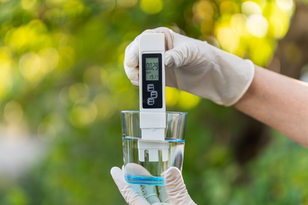 Person in gloves testing water quality with a digital meter in a glass.