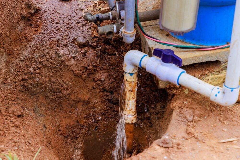 Pipes leaking water in an excavated dirt pit next to a blue water tank.