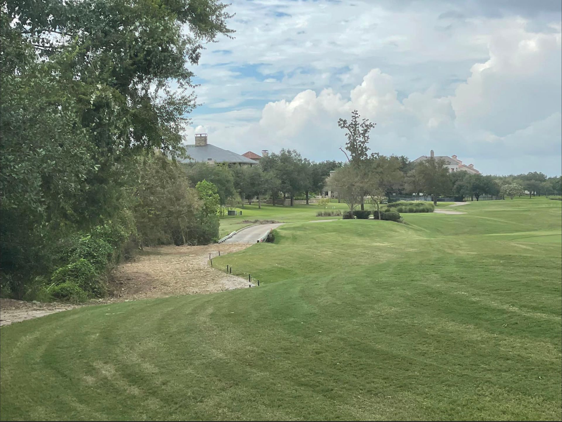 Golf course with green grass, trees, and a cloudy sky. A building is in the background.