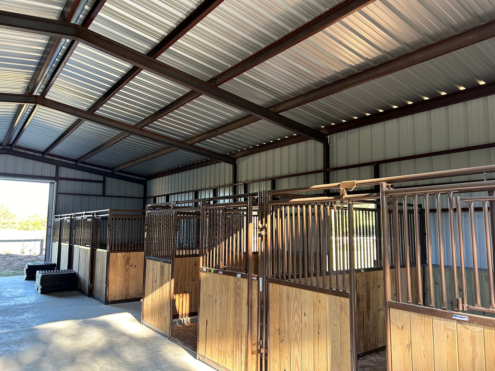Interior of a horse stable with multiple stalls, metal roof, and wooden stall fronts.