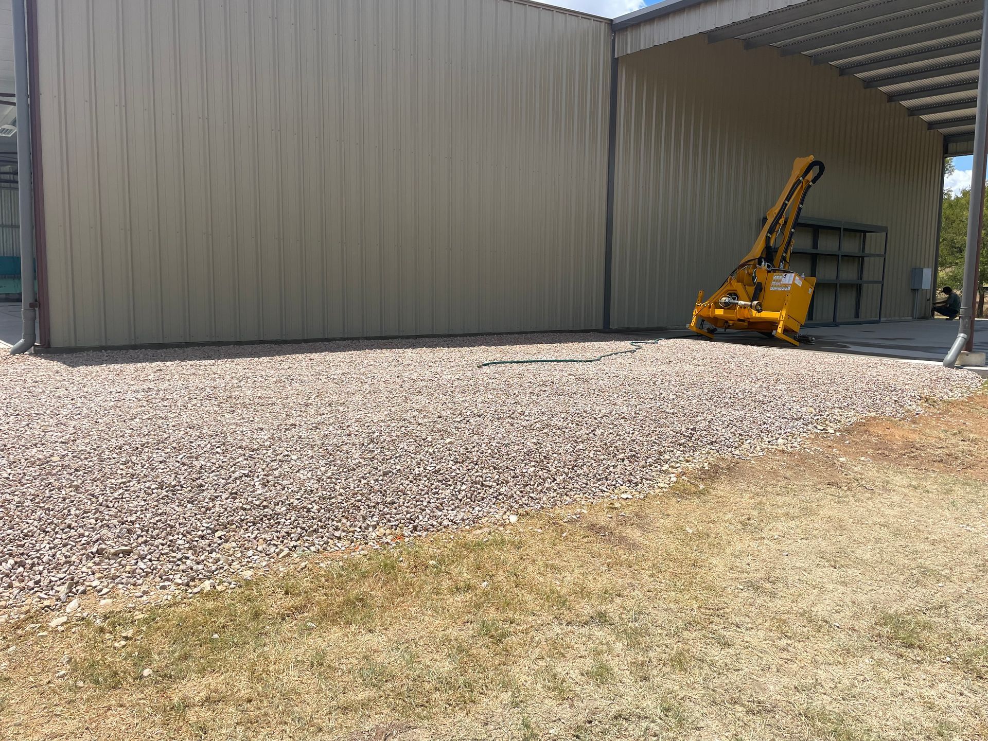 Gravel area next to a tan building, with a yellow machine.