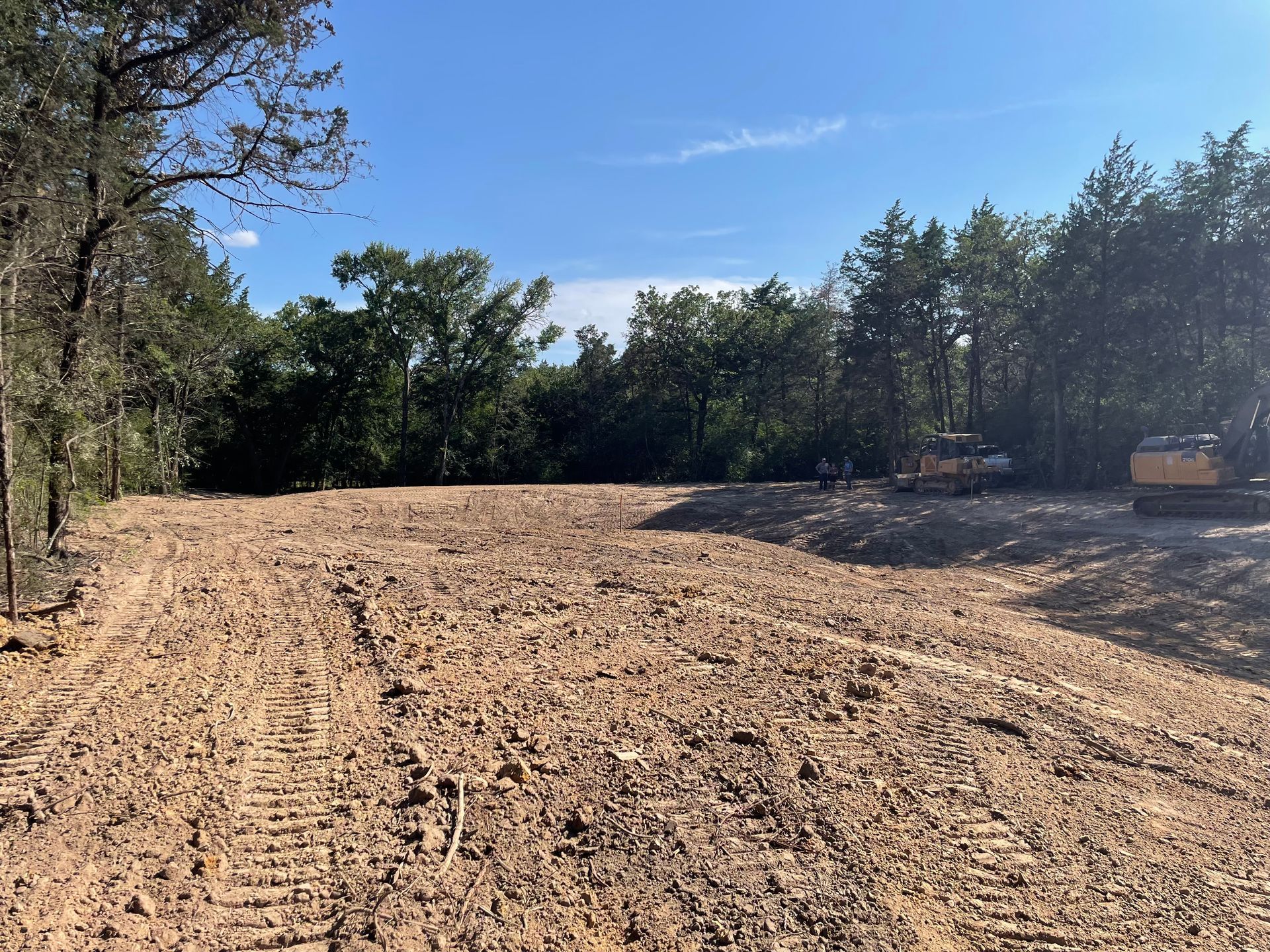 A cleared dirt lot with tire tracks, construction equipment, and trees in the background.