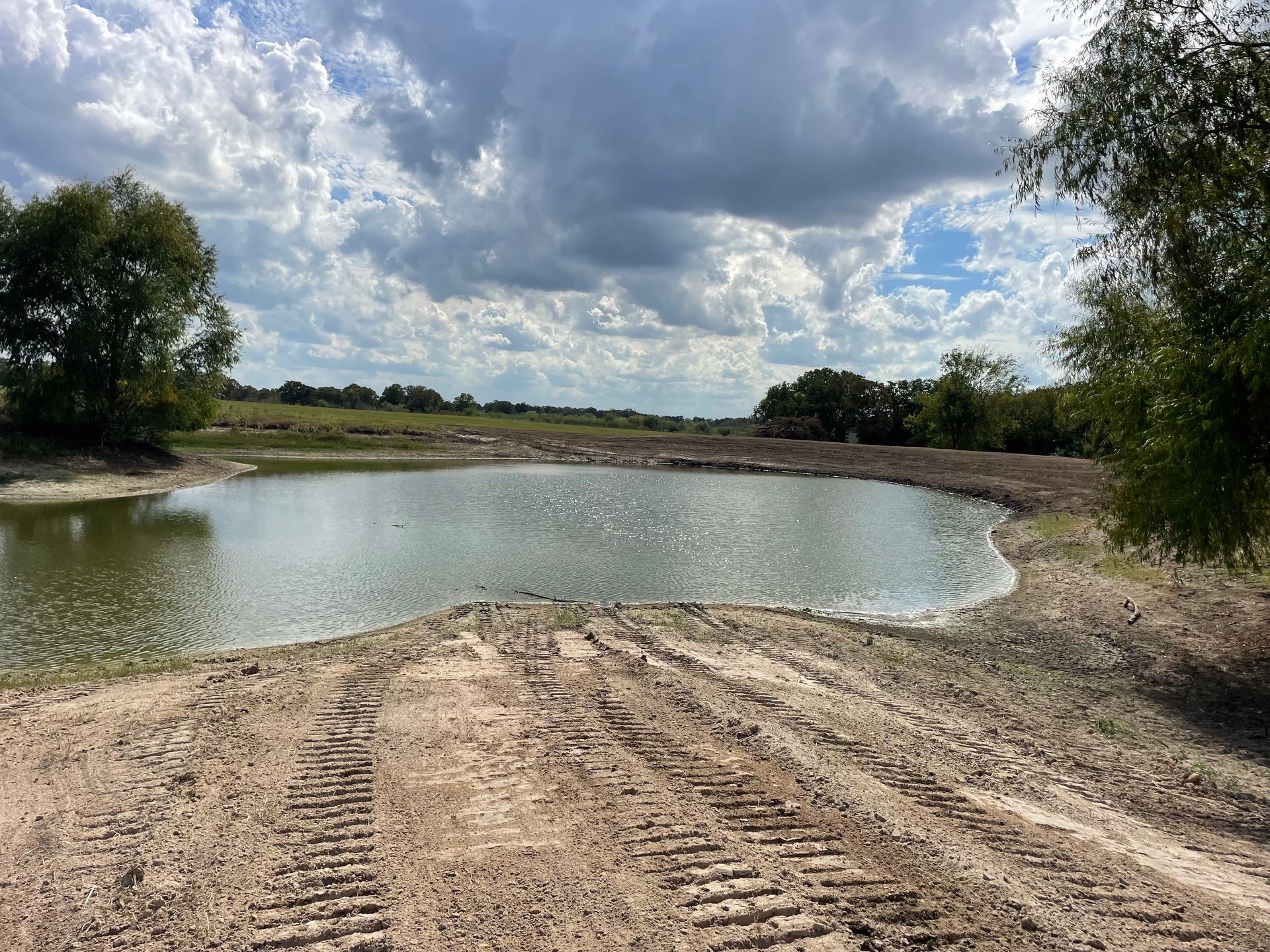 A newly built pond with muddy banks under a cloudy sky. Trees line the edges.