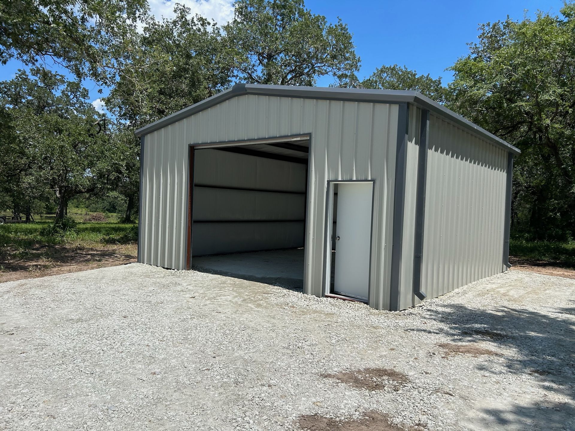 Metal shed with a large open doorway and a smaller door, on a gravel surface.