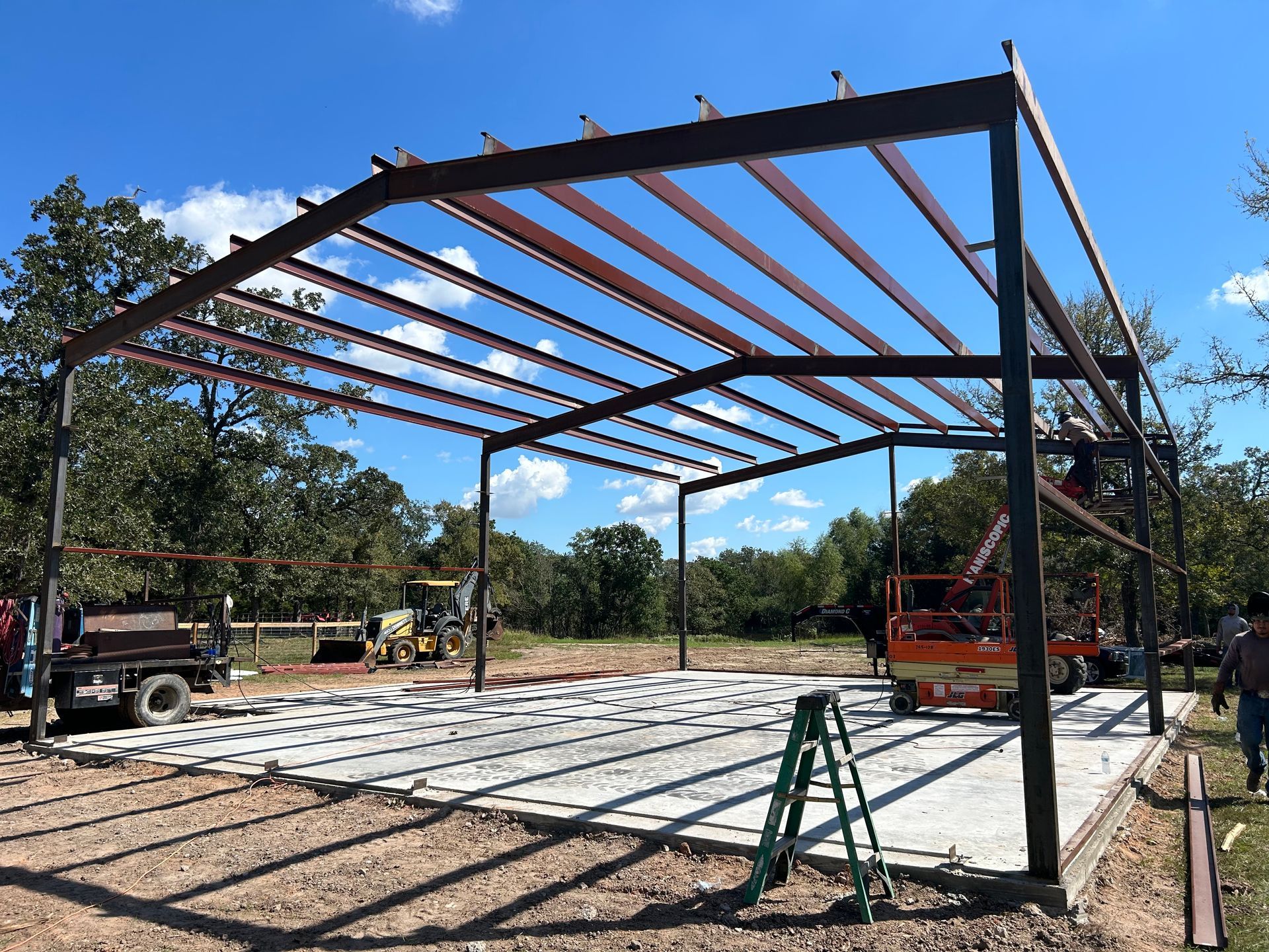 Metal frame of a building under construction on a concrete slab, against a blue sky.