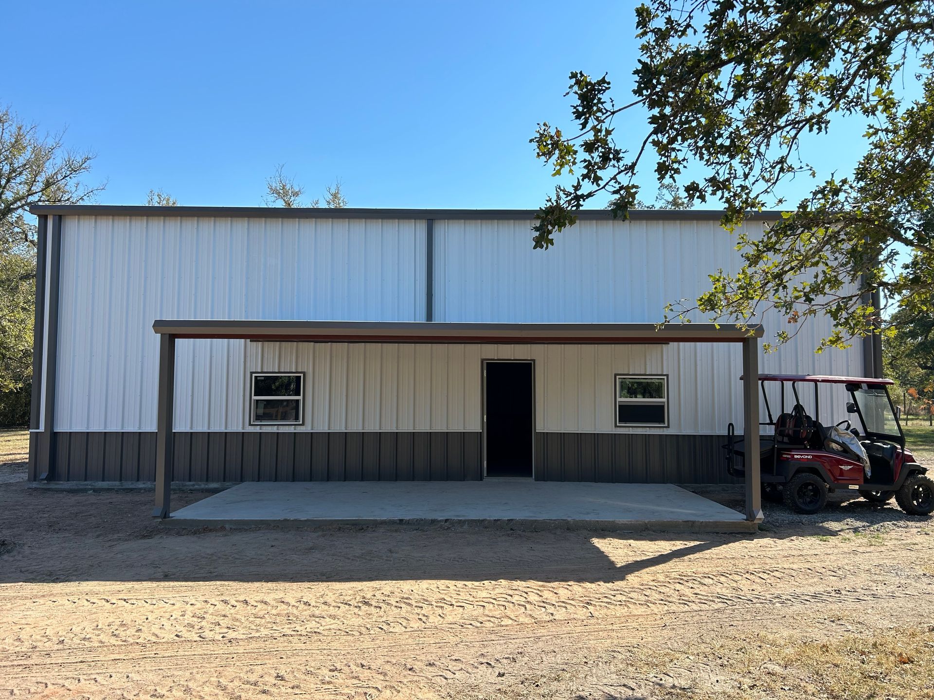 White and brown metal building with covered porch, door, windows, and two red golf carts.