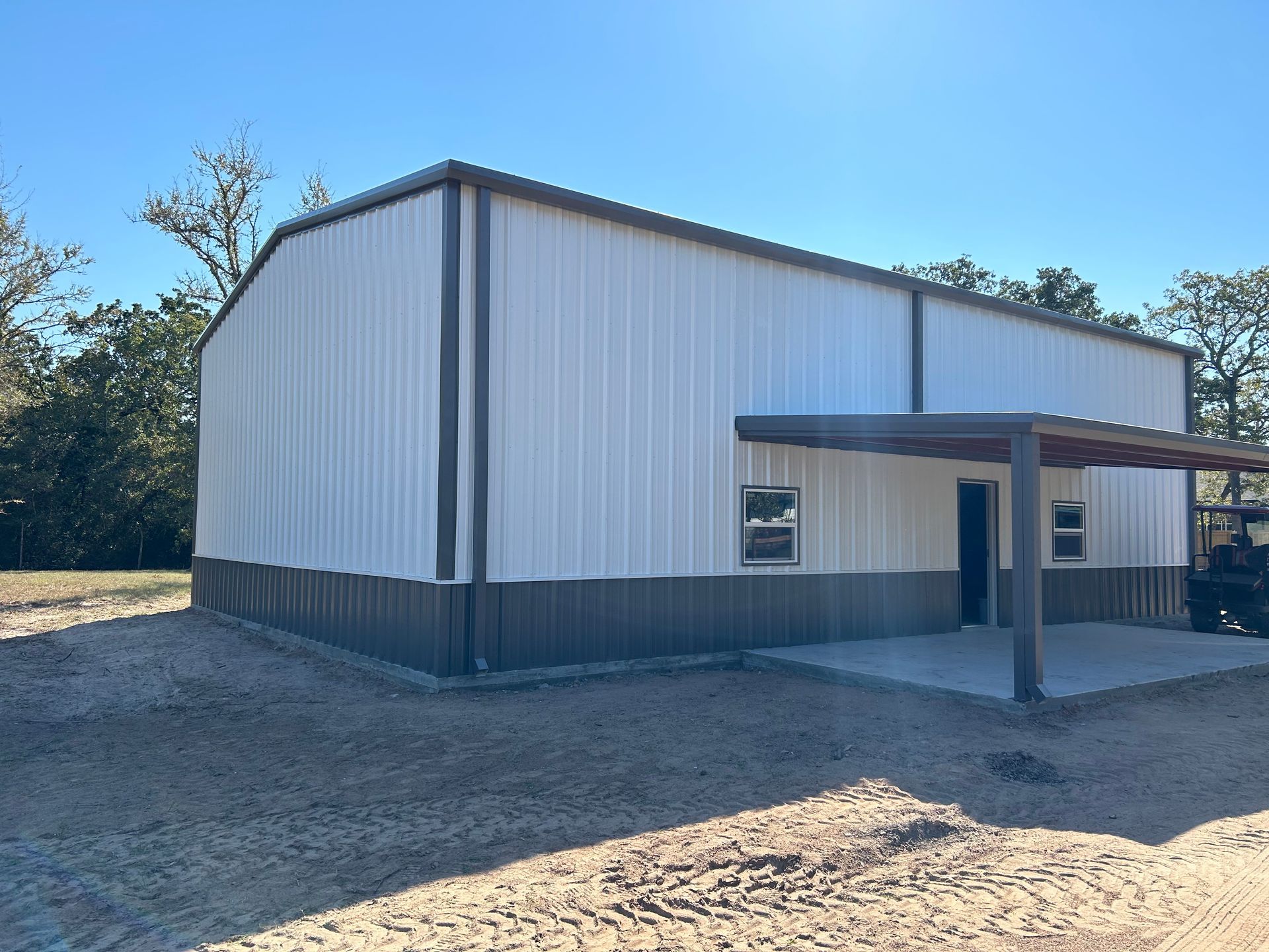 A two-toned metal building with a porch and gravel surrounding it.