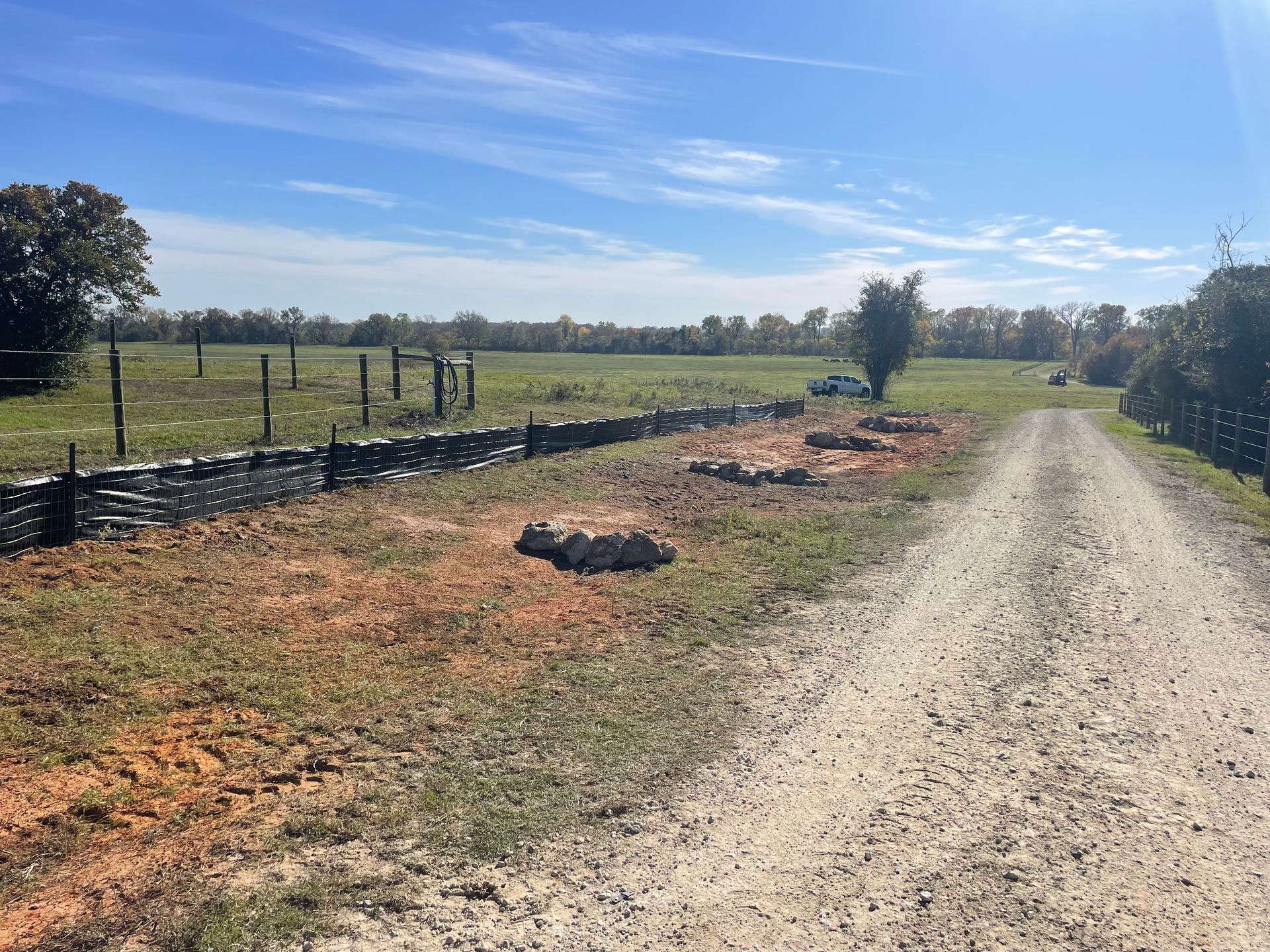 Dirt road leading to a field, flanked by a stone wall and fences, under a blue sky.